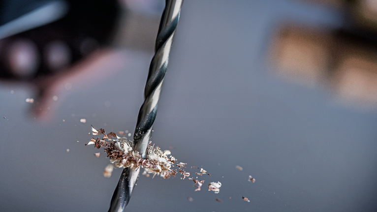 鑽頭在金屬上鑽孔，入口周圍有金屬屑。