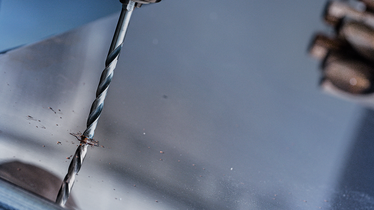 一名穿著安全裝備的人員正在金屬板上鑽孔。