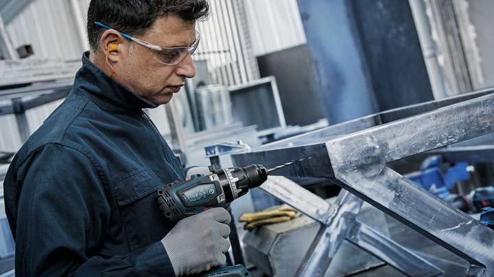 一名穿戴安全裝備的人員正在金屬框架上鑽孔。