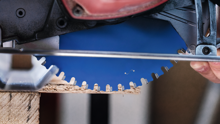 一名操作圓鋸的人正在切割木材，鏡頭特寫展示了鋸片。