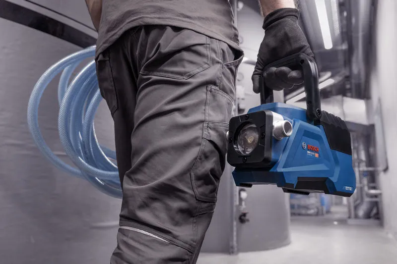 在工業環境中，一名身穿安全裝備的人員攜帶一台藍色便攜式真空幫浦。