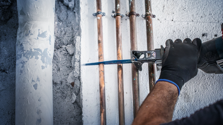 一名穿戴安全裝備的人員使用往復鋸切割混凝土牆上的管道。