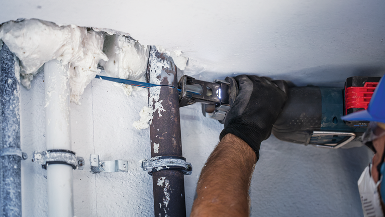 一名穿戴安全裝備的人員使用電動工具切割金屬管。