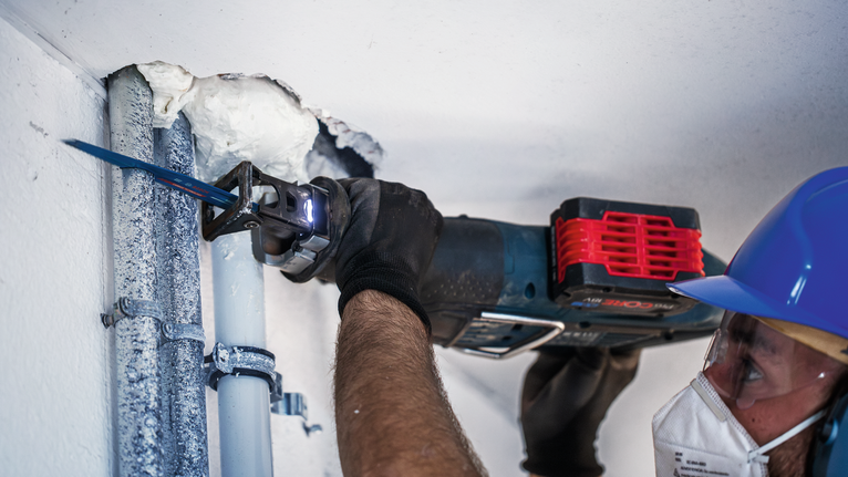 一名穿戴安全裝備的人員使用往復鋸切割天花板管道。