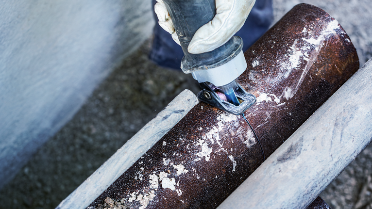 一名穿戴安全裝備的人員使用往復鋸切割一根大型金屬管。