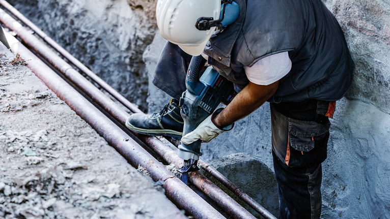 一名穿戴安全裝備的人員在建築工地鑽穿管道。