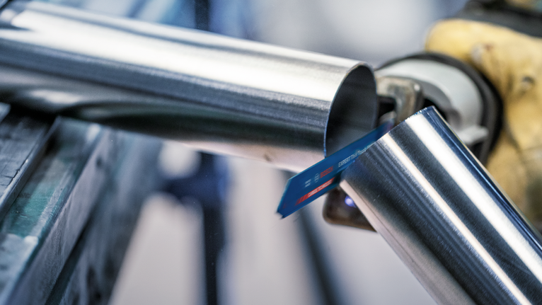 一名穿戴安全裝備的人員用往復鋸切割金屬管。