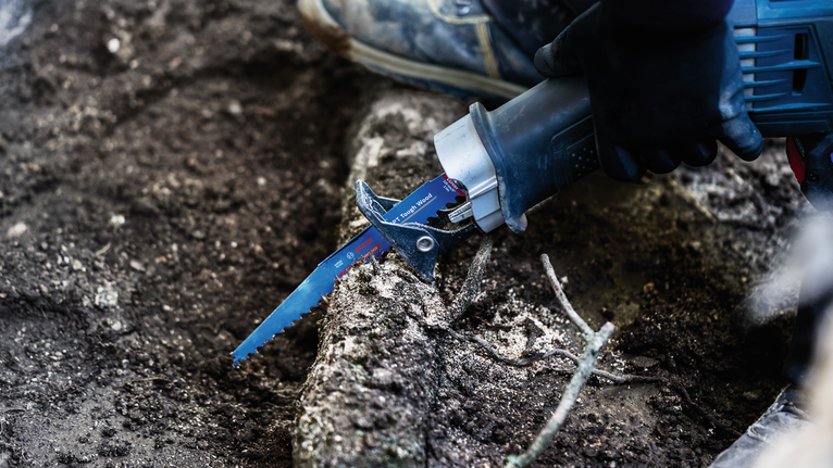 一名穿戴安全裝備的人員用往復鋸鋸斷了一截粗壯的樹根。