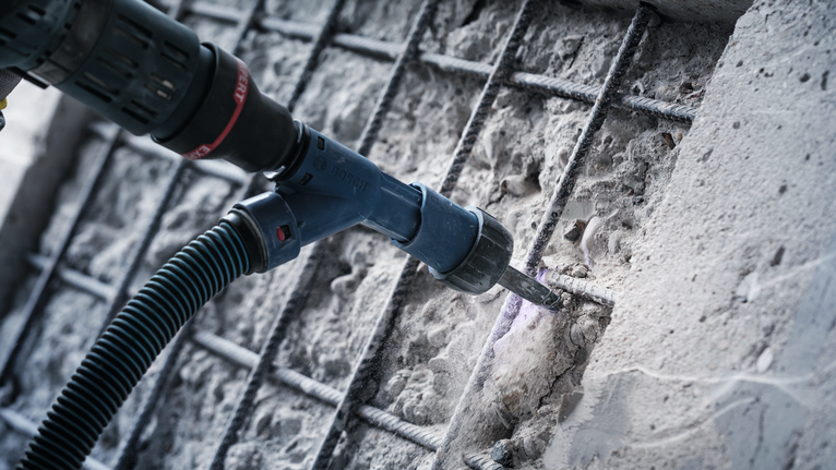 使用電鎚在裸露鋼筋附近的混凝土上鑽孔，並抽取粉塵。