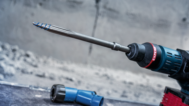 一台裝有長鑽頭和藍色工具部件的旋轉衝擊鑽在混凝土表面上作業。