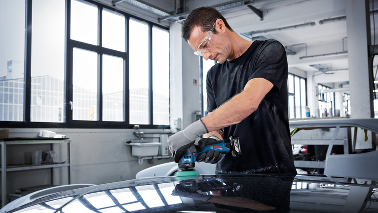一名配戴安全裝備的人員使用無線電動工具打磨汽車表面。