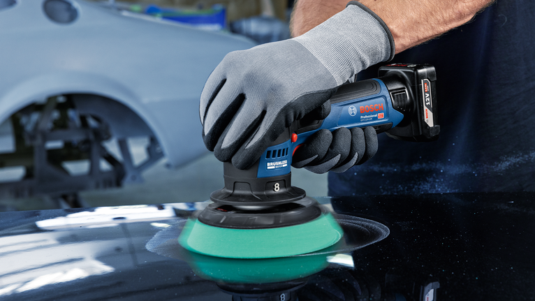 一名穿戴安全裝備的人員使用無線工具拋光汽車錶面。