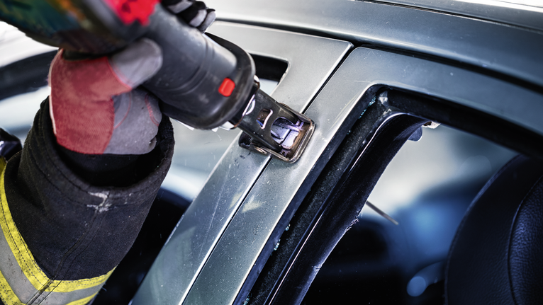 一名配戴安全裝備的人員使用電動工具切割汽車車架。