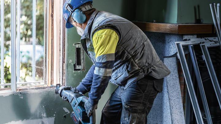 一名配戴安全裝備的人員使用電動工具切割窗框。