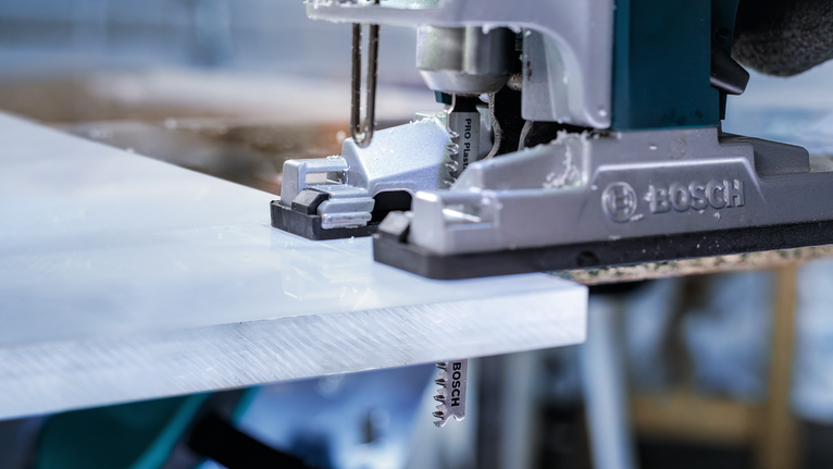 在車間裡用曲線鋸切割白色塑膠板。