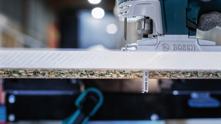 車間裡，一把曲線鋸正在切割一塊層壓木板。