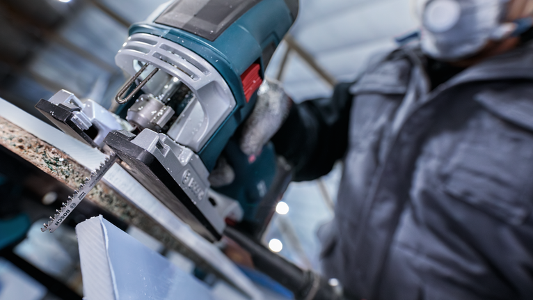 配戴安全裝備的人員使用曲線鋸切割一塊材料。