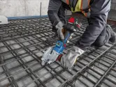 一名穿戴安全裝備的人員使用無線工具在建築工地切割鋼筋。