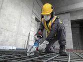 一名穿戴安全裝備的工人正在使用無線鋼筋切割機切割鋼筋。