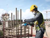 一名穿戴安全裝備的人員正在建築工地使用無線工具切割鋼筋。