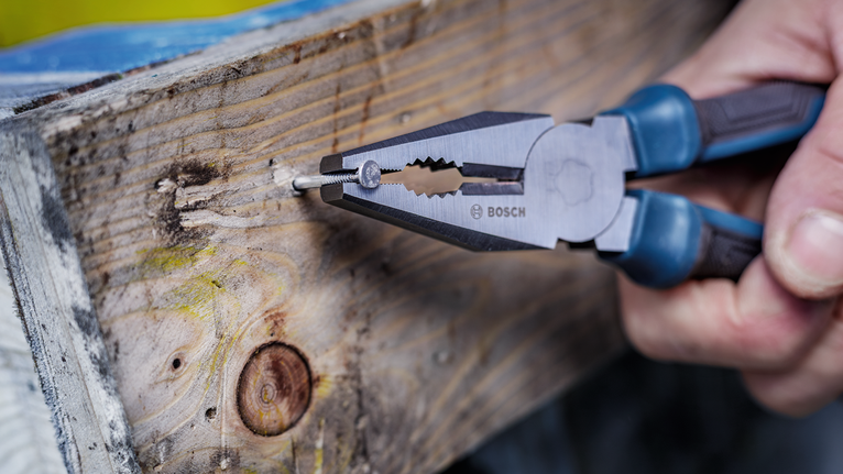 人用鉗子夾住木板上的釘子。