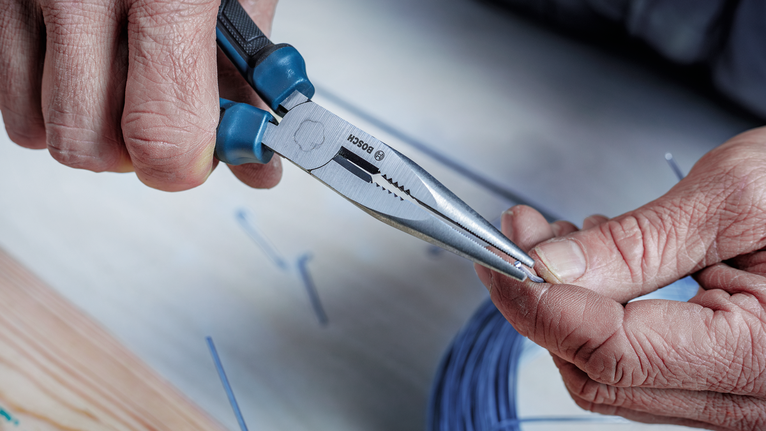 有人用尖嘴鉗扭細鐵絲。