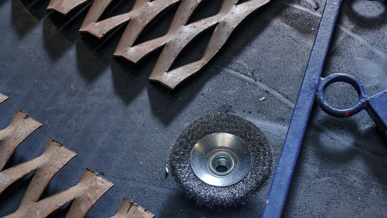 鋼絲刷盤放在工作台上，旁邊是金屬切割件和藍色工具。