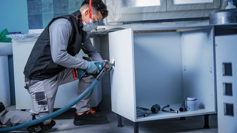 一名穿戴安全裝備的人員使用電動工具在廚具上開孔。