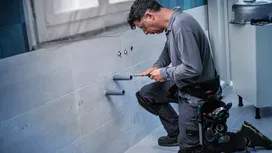 一名穿戴安全裝備的人員正在磁磚浴室牆上安裝管道。