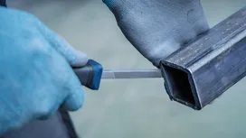 穿戴安全裝備的人員正在銼削金屬方管的邊緣。