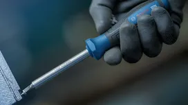配戴安全裝備的人員將螺絲起子旋入金屬表面。