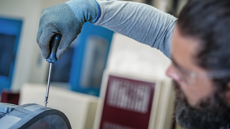 穿戴安全裝備的人員正在擰緊金屬外殼上的螺絲。