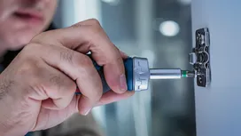 有人正在使用電動螺絲起子在櫥櫃門上安裝鉸鏈。