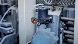 穿戴安全裝備的人員正在用棘輪扳手擰緊工業機械上的螺栓。
