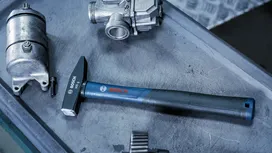 一把藍色手柄的鐵鎚放在金屬工作台上，旁邊是汽車零件。