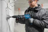 一名配戴安全設備的人使用電動工具在混凝土牆上鑽了一個大洞。