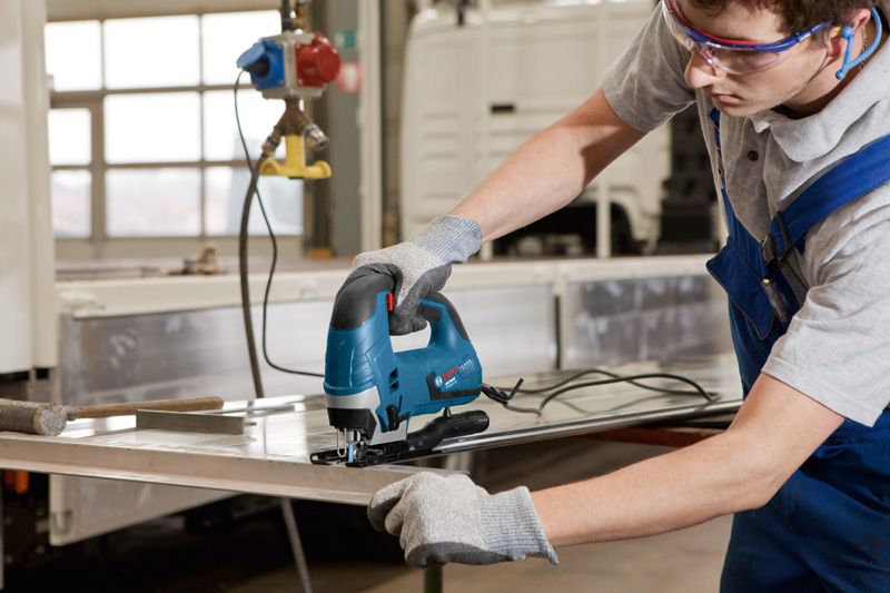 配戴安全設備的人使用曲線鋸切割金屬板。.