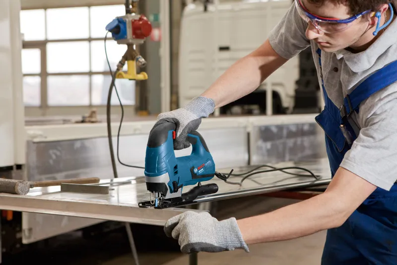 配戴安全設備的人使用曲線鋸切割金屬板。.