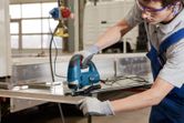 配戴安全設備的人使用曲線鋸切割金屬板。.