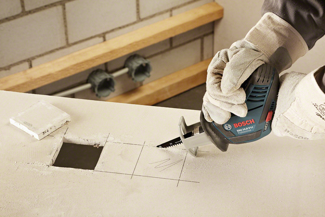 戴著安全設備的工人使用往復鋸在乾牆上切出一個方形孔。.